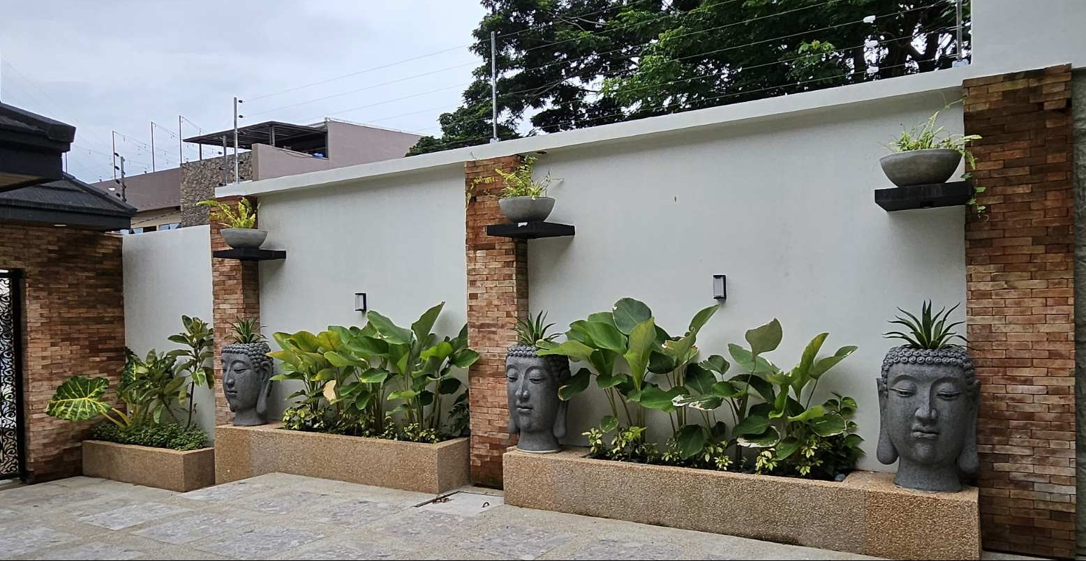 Three Buddha-head planters among tropical planting along the courtyard wall.