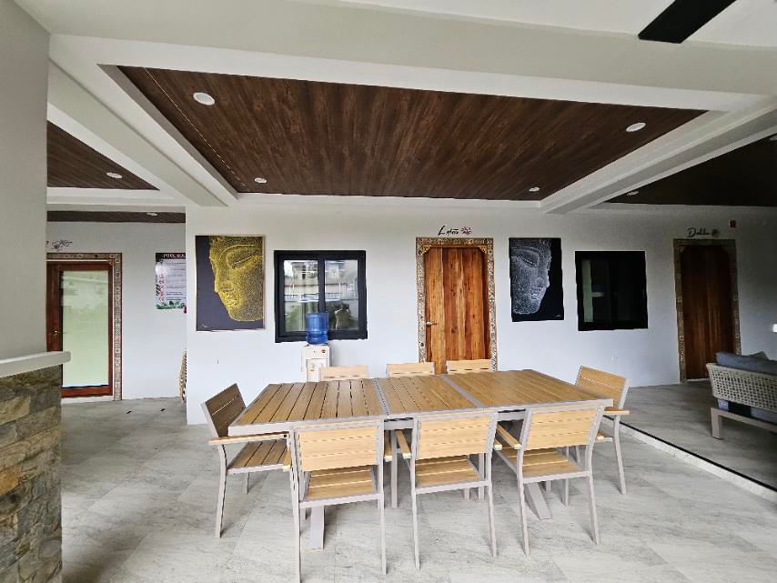 Wooden dining tables and chairs beneath a wood-paneled ceiling, with guest-room doors behind.