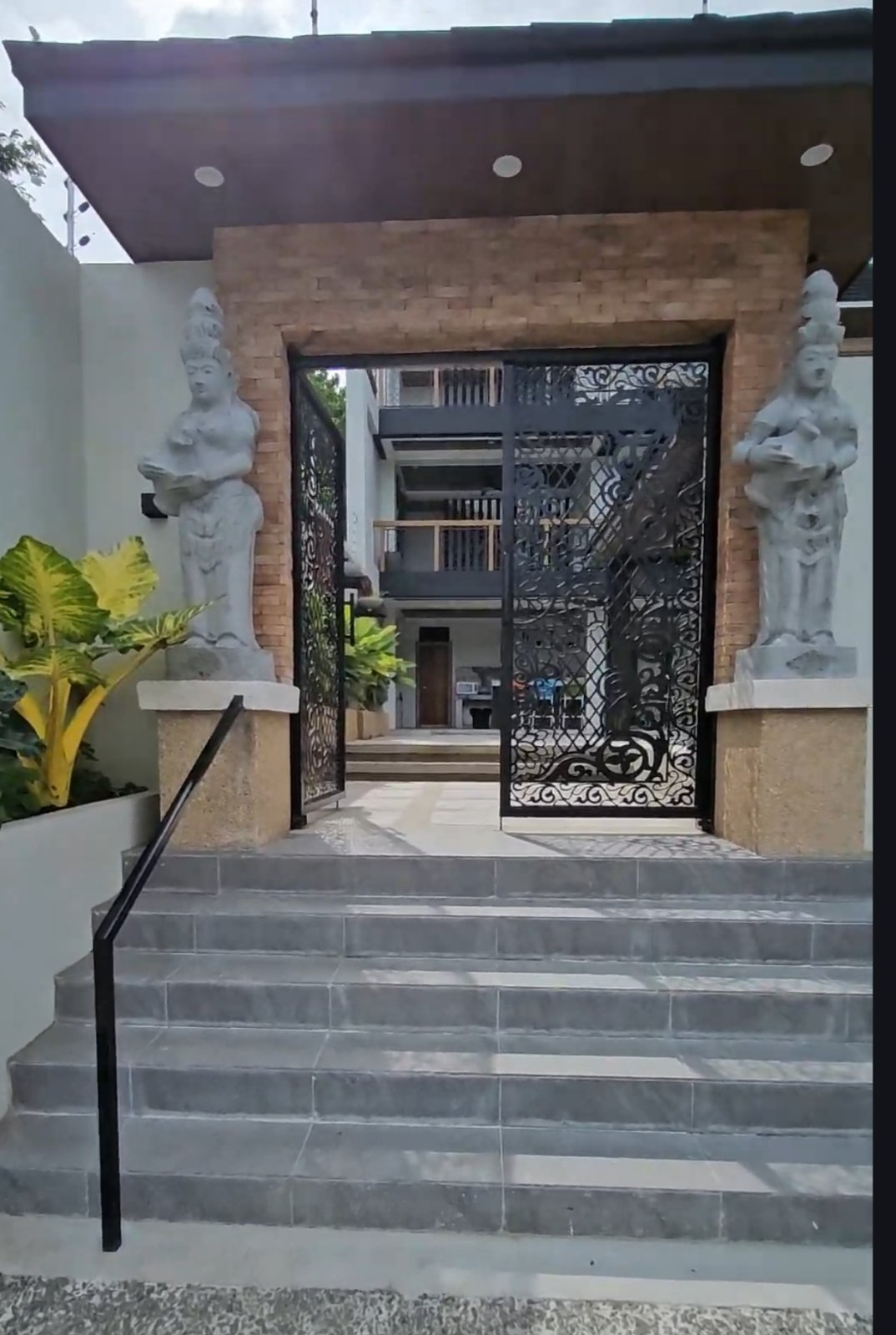 Stone steps lead to an ornamental black gate flanked by two statues.