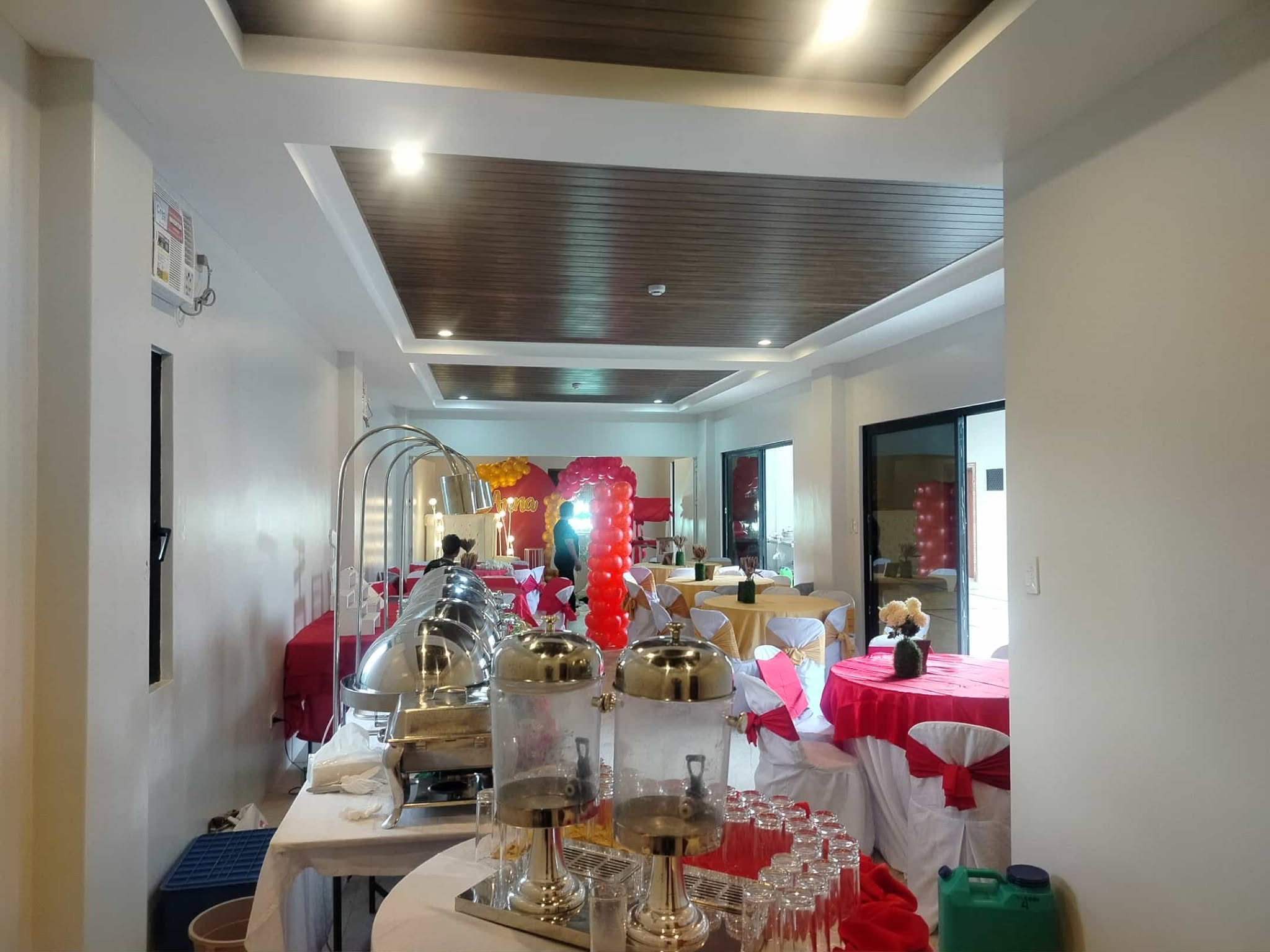 Function room arranged with buffet chafing dishes, drink dispensers and red-and-gold event tables.