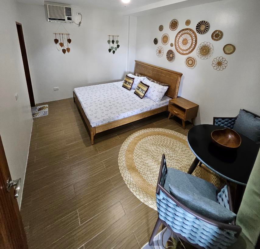 Lilac room with a wooden bed, woven wall decorations and a two-chair sitting corner.