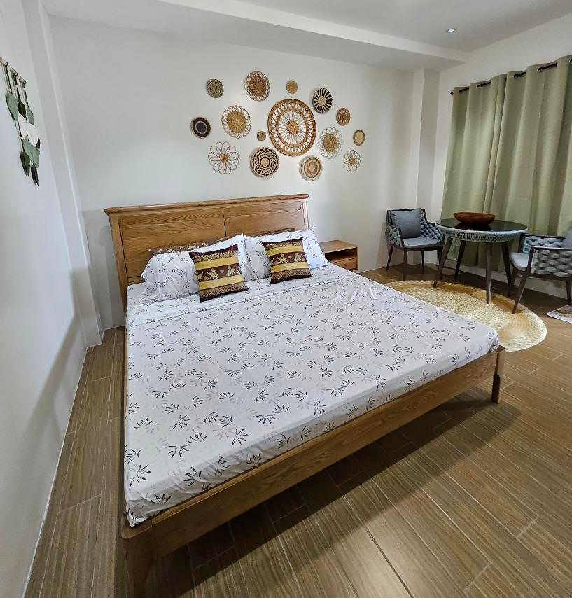 Wooden bed with patterned linens beneath woven wall decorations in the Lilac room.