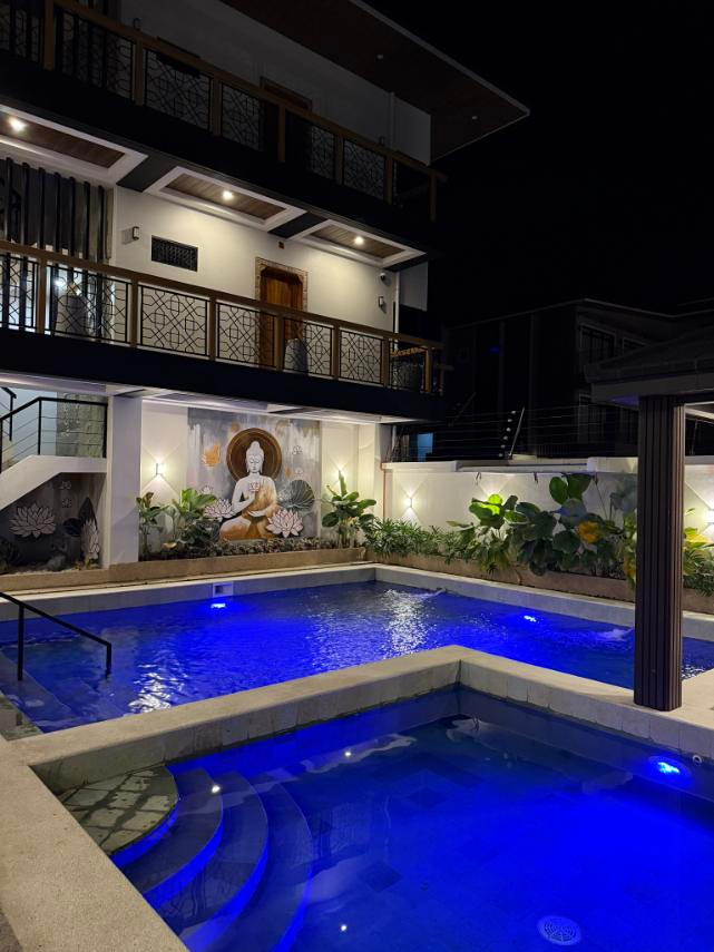 Pool water illuminated in blue at night beneath balconies and the Buddha mural.