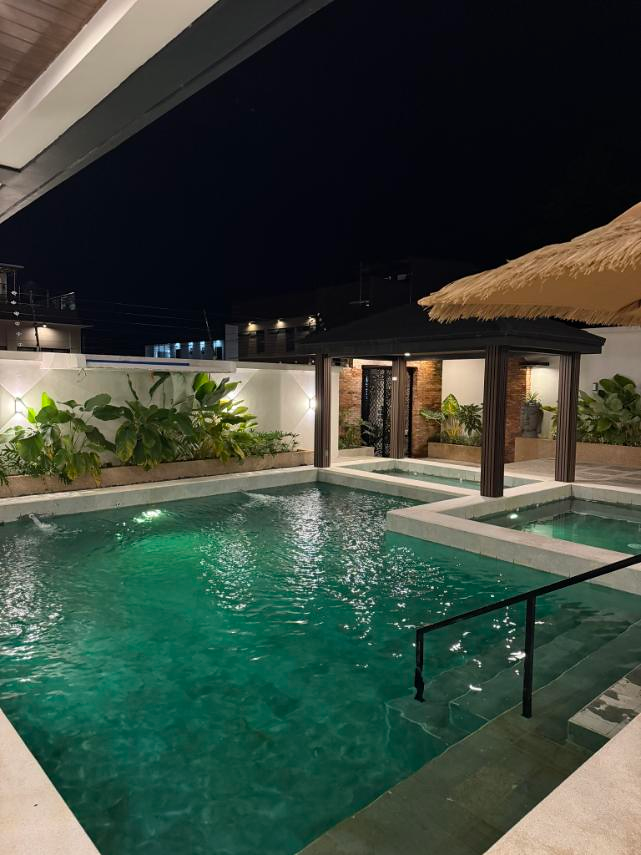 Nighttime pool view with green lighting, entry steps, a handrail and the pavilion.