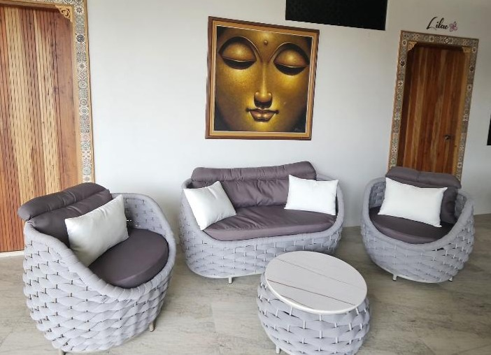 Woven sofa and armchairs with a round table beneath framed Buddha artwork.