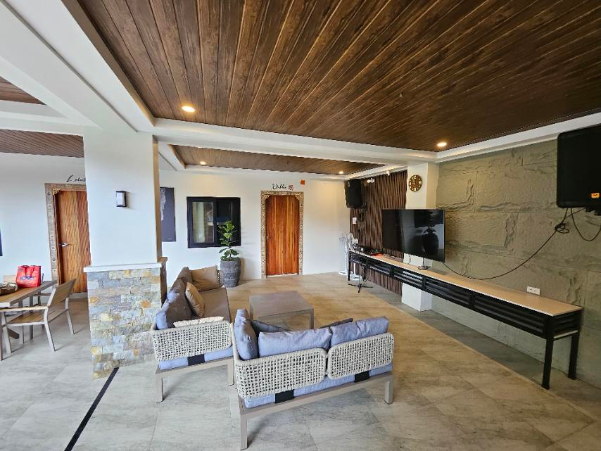 Covered lounge with woven sofas, a television and mounted speakers.